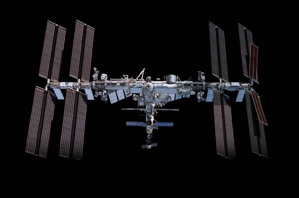 Aerial view of the International Space Station (ISS) against a black background, showcasing its solar panels and various modules.